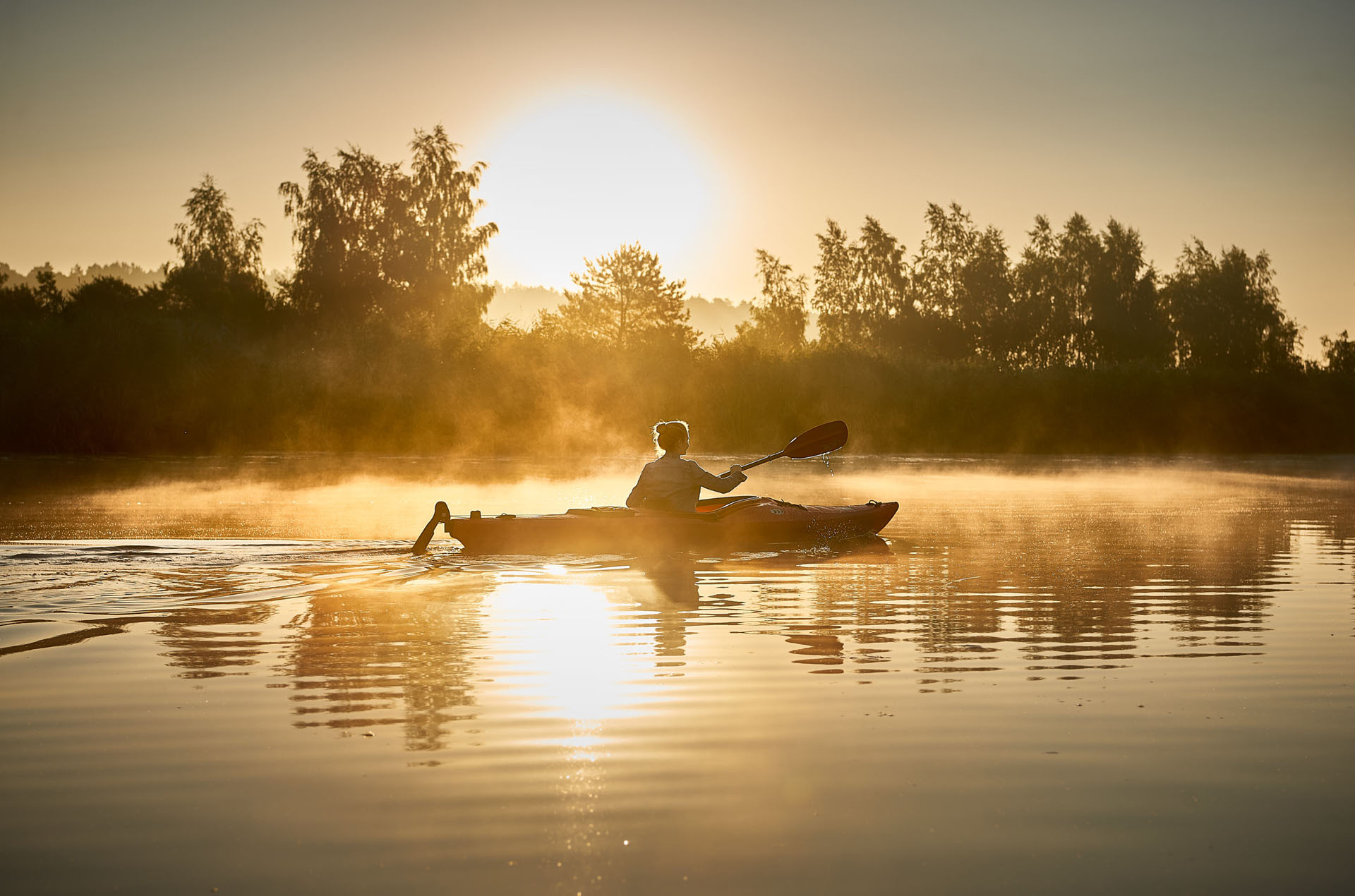 Ein Kajak auf dem Fluss von der Seite in Morgen Stimmung. Nebel kommt vom Fluss hoch.